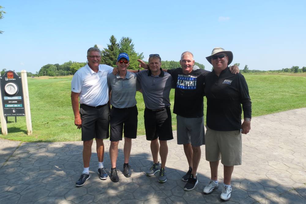 Five football alums standing in front of the golf course.
